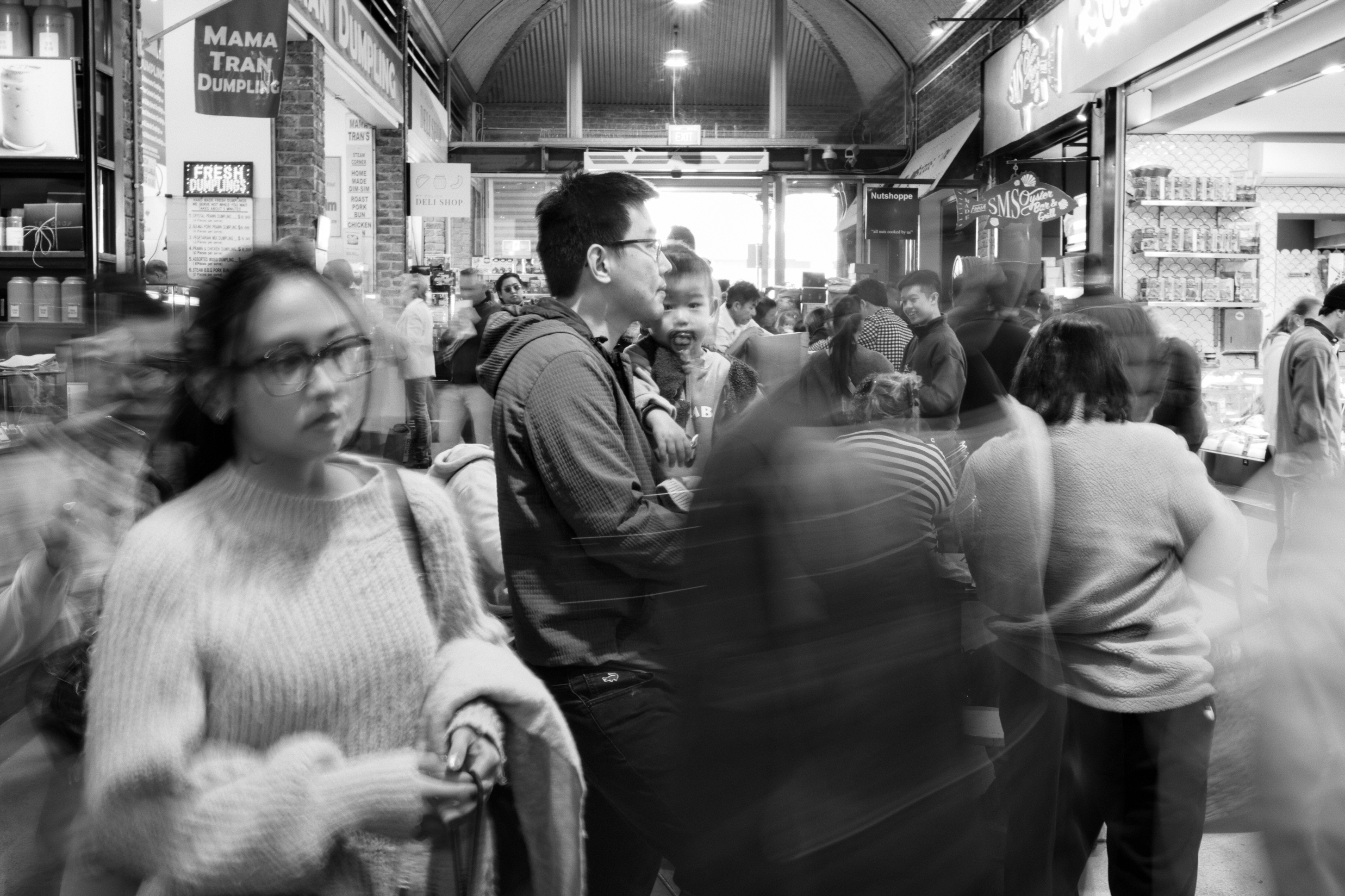 Black and white photograph of a man holding his child in the bustling South Melbourne Market.