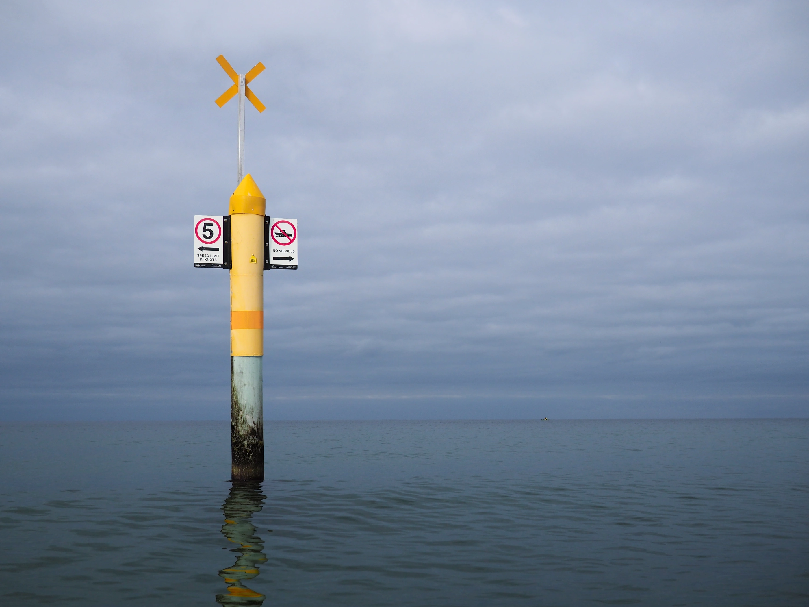 A yellow marker indicating an area restricted for vessels near Aspendale beach. The sky is overcast make the sea water appear in dark grey.