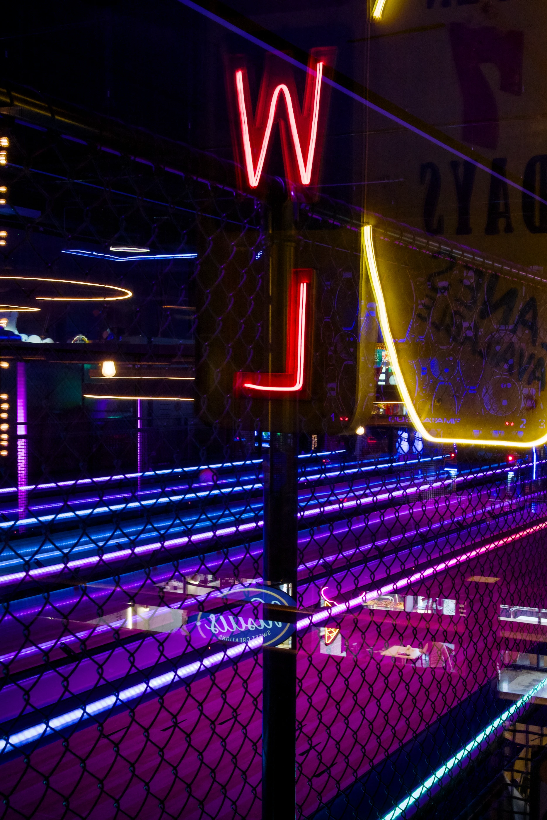 An abstract photograph from a bowling alley. The lanes are lit in pink and blue tones. In the front is a stylised bowling pin and the letters W and L.