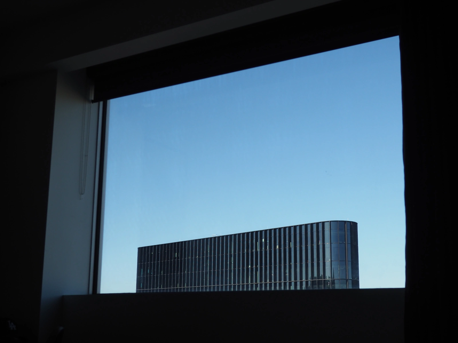 View trough a window on the top of a building across the road. The building has a glass front and black frames. The sky is bright blue.